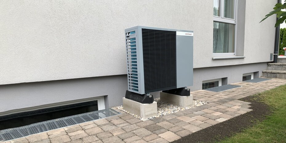 Außenaufgestellte Wärmepumpe an einem Mehrfamilienhaus, installiert auf stabilen Fundamentblöcken | © bösch
