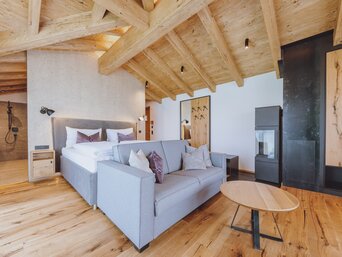 Innenansicht eines Zimmers im Hotel-Dorf Zaglgut mit sichtbarer Holzbalkendecke, Echtholzboden, Kamin und natürlichen Materialien wie Stein und Loden – für ein gemütliches, alpines Wohngefühl. | © Hotel & Chalets Zaglgut
